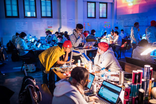 Rows of people working on laptops in a colourfully lit hall