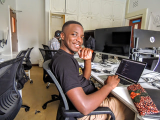 A software developer smiling at his desk beside a laptop showing code