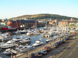 Boats moored in Swansea Marina on a sunny evening, with a green hill behind