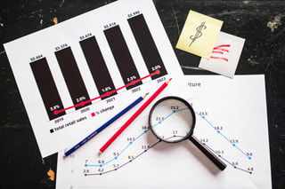 Printed sales charts with a magnifying glass, pencils and a note on a dark desk