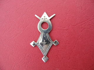 A silver Agadez cross pendant lying on red leather
