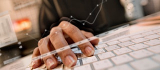 A hand typing on a keyboard with charts and data overlaid